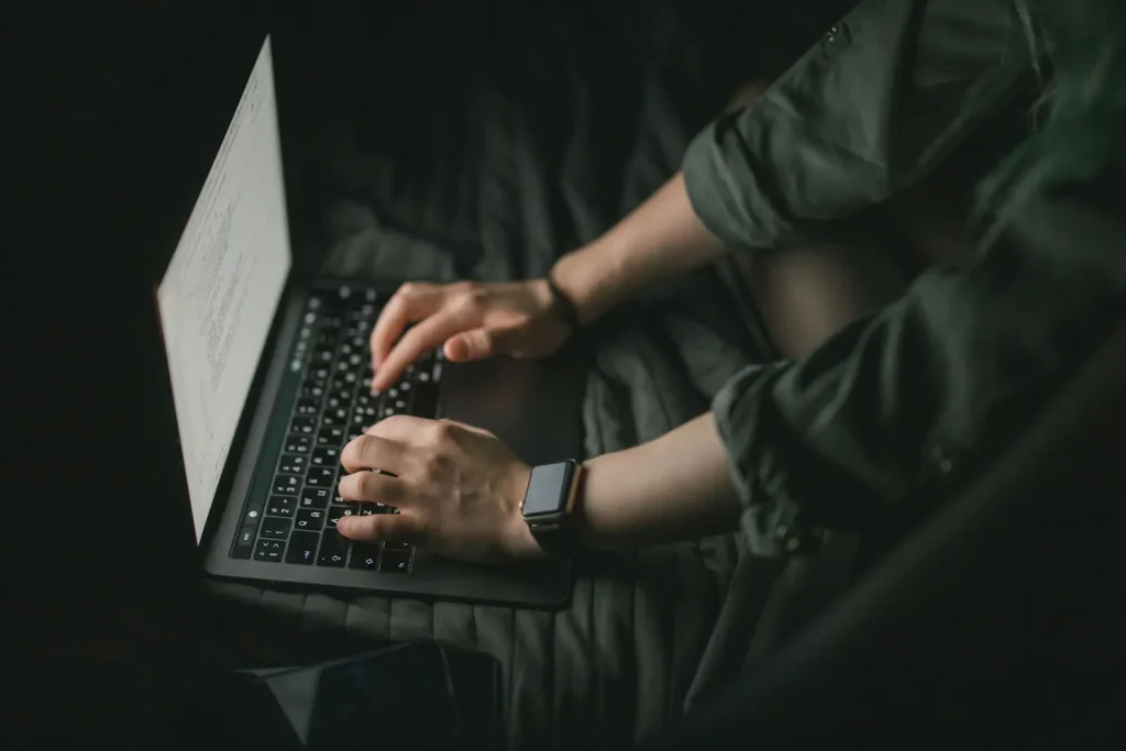 Mâini care tastează pe un laptop într-o cameră întunecată