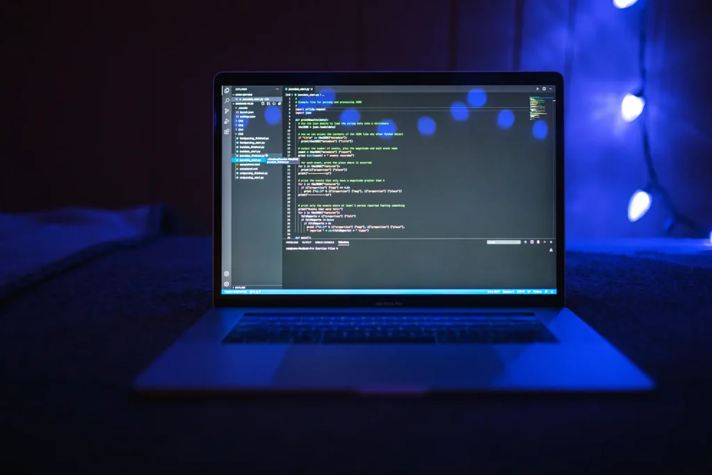 Laptop showing program code in a dark room lit in blue